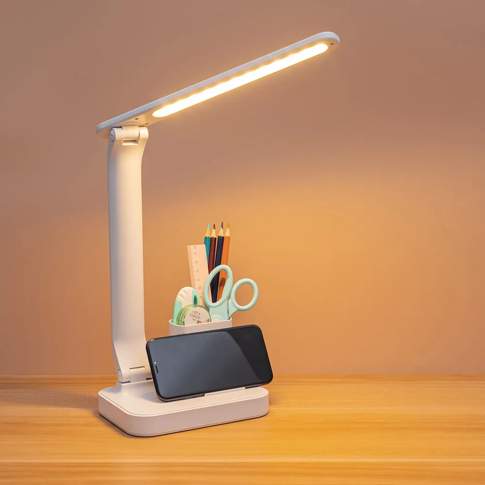 Flexo led blanco regulable base portalápiz Bosco Fabricado en ABS con portalápiz en su base y una bandeja para depositar clips, goma, etc. También posee de un filo donde reposar su dispositivo móvil en posición idónea para su visualización tanto arriba como en la bandeja. Su iluminación es de led integrado con una potencia de 6 watios, 450 lúmenes y tres tonos de luz 3000ºK(cálida), 4500ºK(neutra) y 6000ºK(fría) regulable en intensidad de luz e interruptor táctil